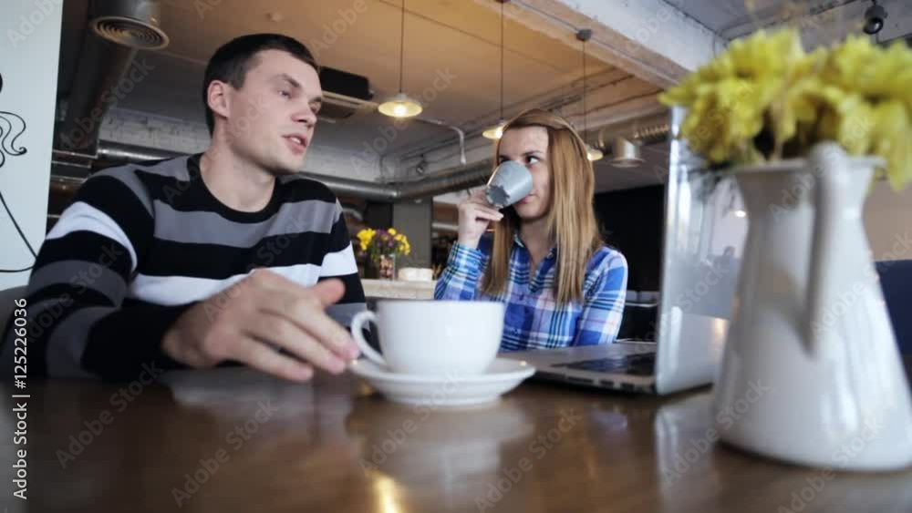 Two friends sitting in cafe, talking, drinking coffee and using laptop Two friends sitting in cafe, talking, drinking coffee and using laptop