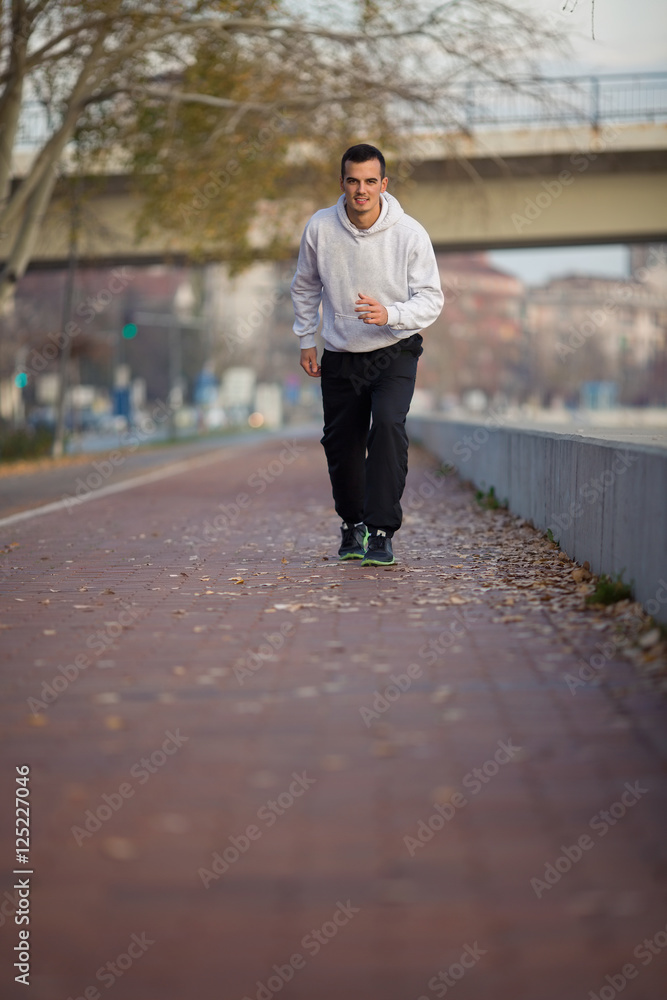 Attractive young man is jogging on the quay by the river