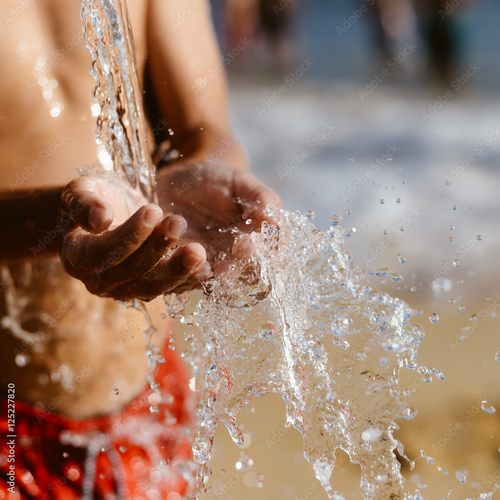 Fototapeta premium Hand and water, wet sand blurry outdoors background, close up image