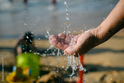 Hand and water, wet sand blurry outdoors background, close up image