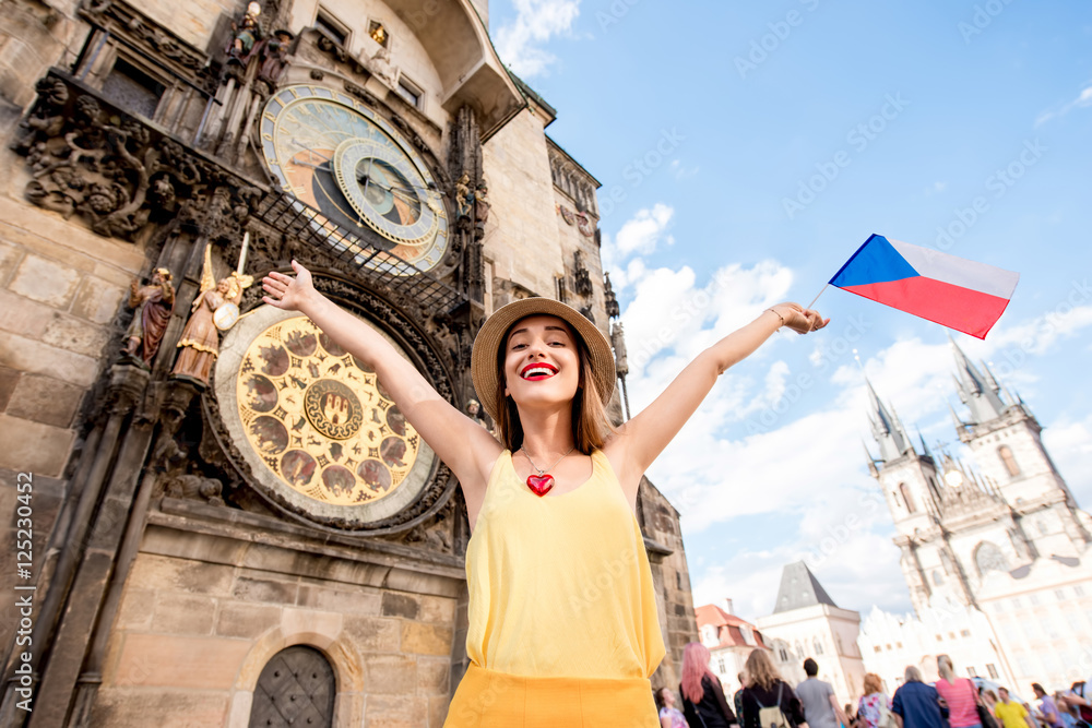 Naklejka premium Young female tourist with czech flag in front of the famous astronomical clock in Prague