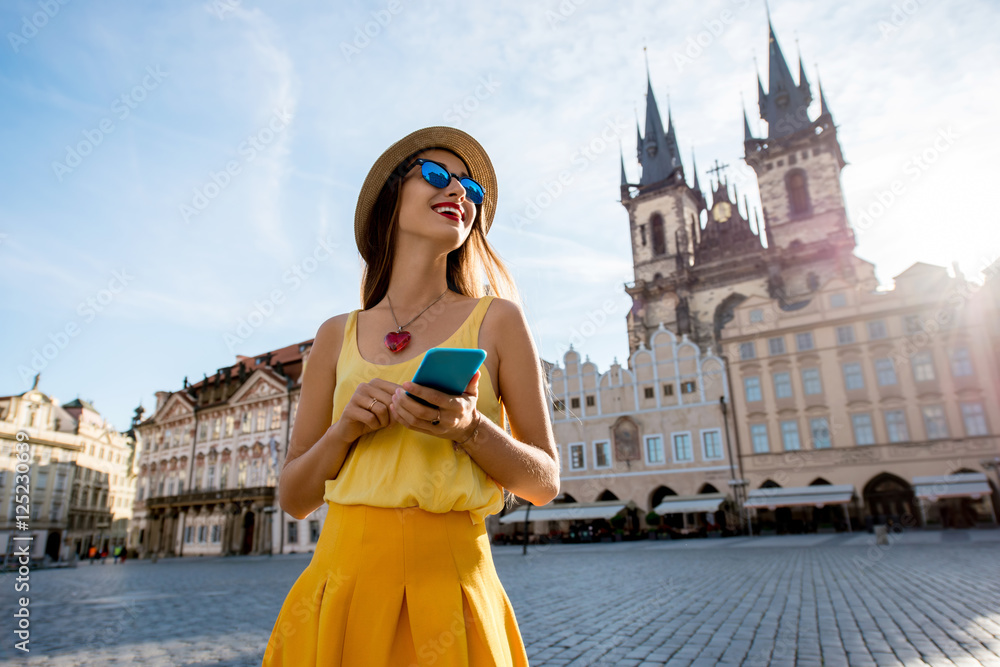 Naklejka premium Młoda kobieta w żółtym spaceru z inteligentnego telefonu na rynku starego miasta w Pradze