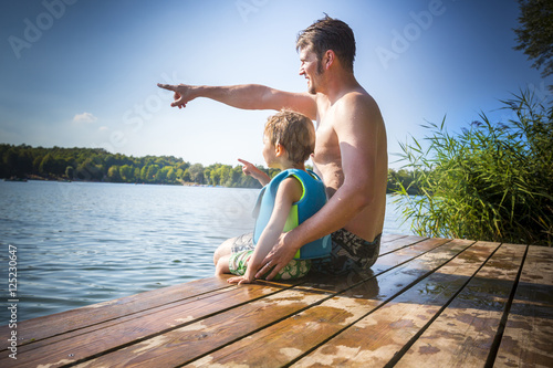 Father and son together sitting on a lake #125230647