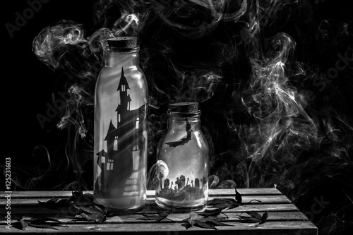 Spooky Halloween scene with castle and cemetery decorations in bottles with smoke in black and white colours.