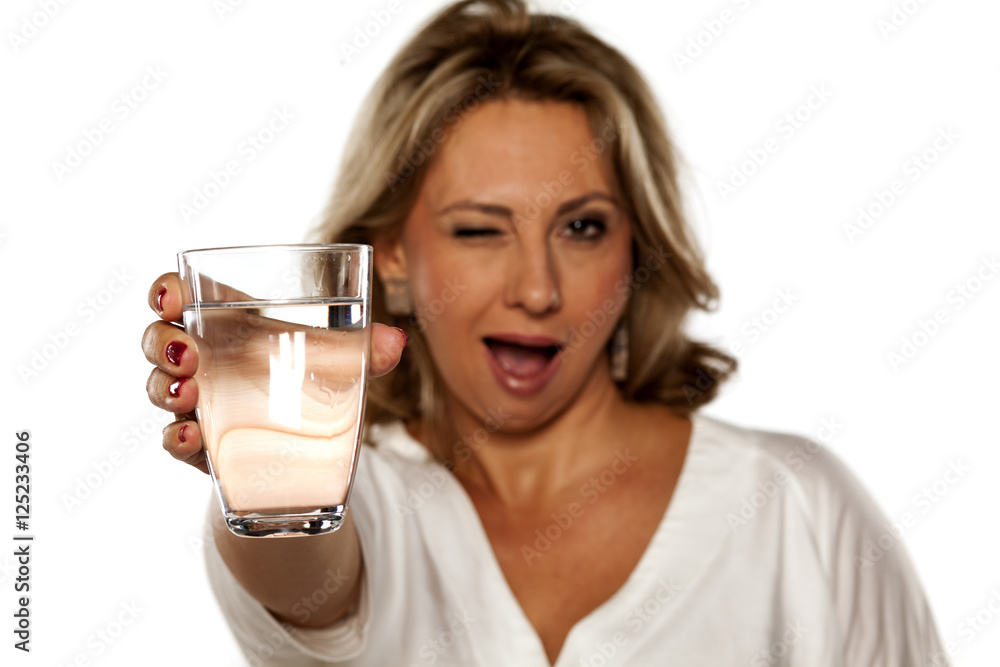 smiling middle-aged woman holding a glass with water and winking smiling middle-aged woman holding a glass with water and winking