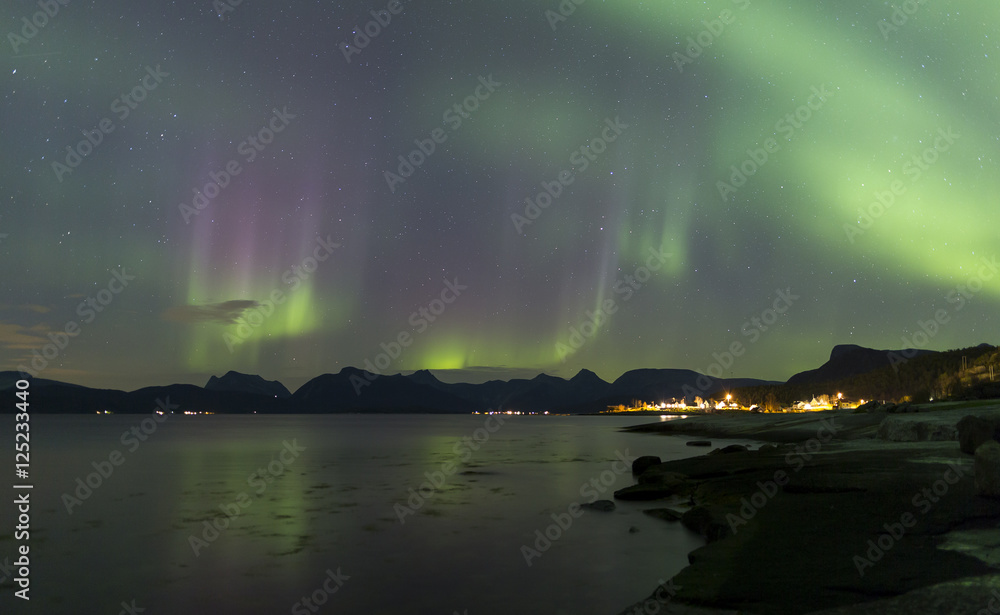 purple and green aurora over fjord with village lights purple and green aurora over fjord with village lights