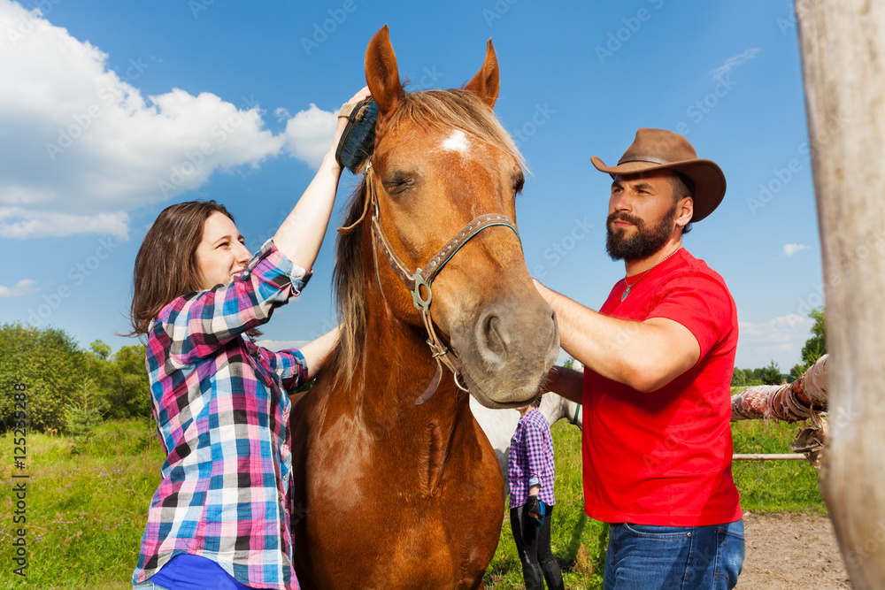 Happy young couple brushing mane of their horse