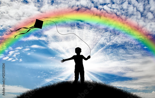 Boy plays with a kite on the street day and rainbow