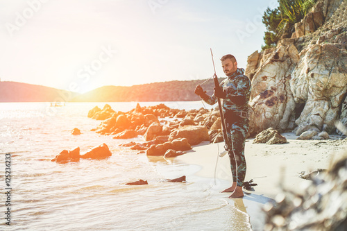 Young man preparing speargun for underwater fishing at sunset 
