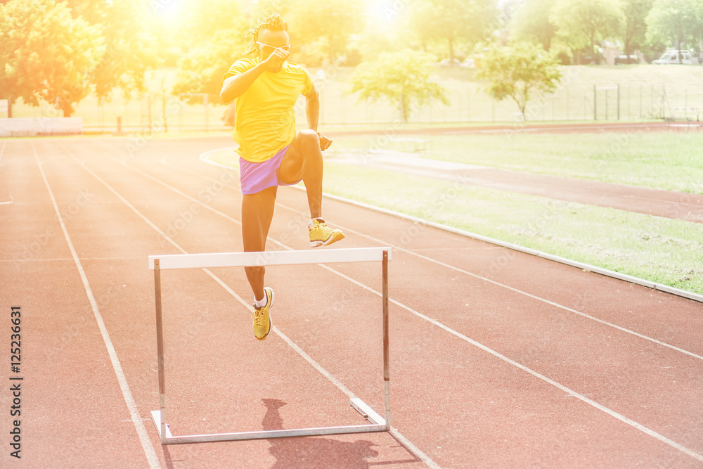 Fototapeta premium African athlete jumping hurdle in a athletic running track