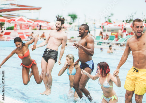 Group of multiracial friends jumping inside swimming pool in aqua park