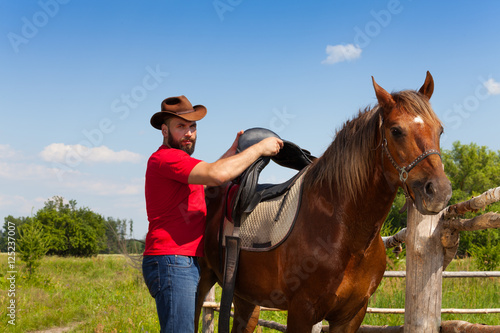 Man in cowboy hat saddling his beautiful horse