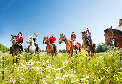 Duża grupa jeźdźców konnych na kwiecistej łące