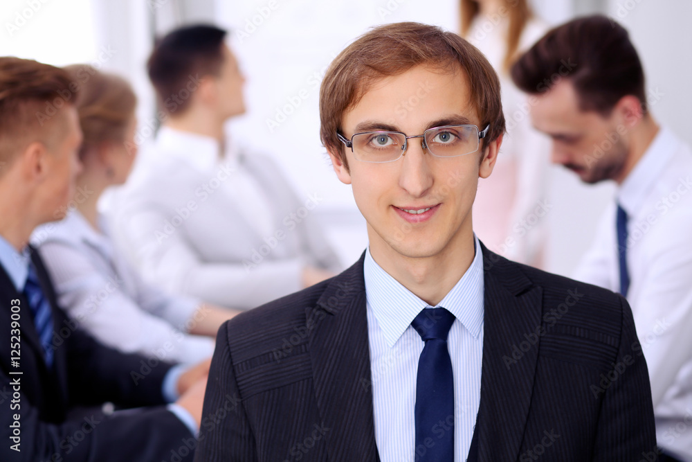 Portrait of cheerful smiling businessman  against a group of  people at meeting.