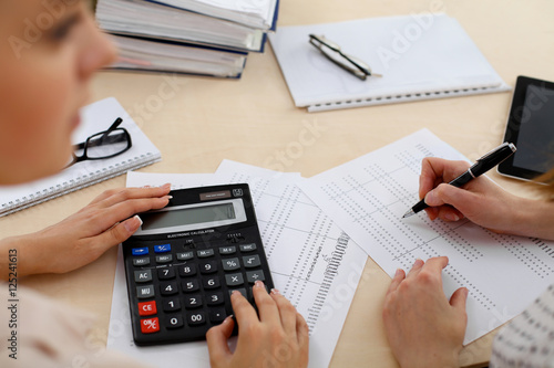 Two female accountants counting on calculator income for tax form completion hands closeup. Internal Revenue Service inspector checking financial document. Planning budget, audit concept