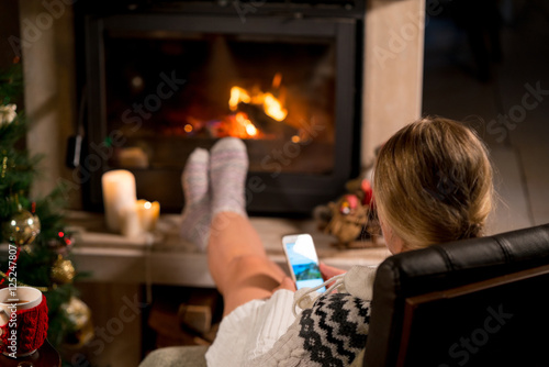 Woman is sitting with phone near the fireplace