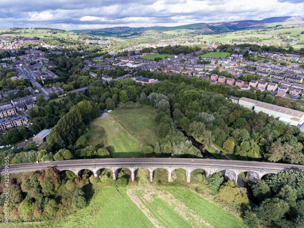 Aerial view of the village railway going across the bridge over path, river and green fields, New Mills, Derbyshire