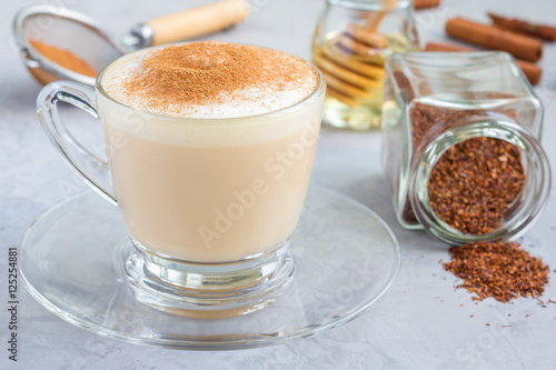 Healthy rooibos red tea latte topped with cinnamon, in glass cup and ingredients on background, horizontal