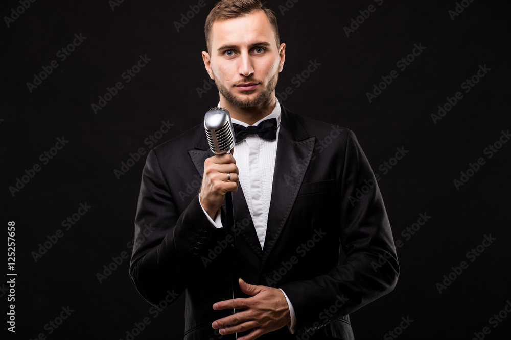Young man in suit singing over the microphone with energy. Isolated on dark background. Singer concept. Young man in suit singing over the microphone with energy. Isolated on dark background. Singer concept.