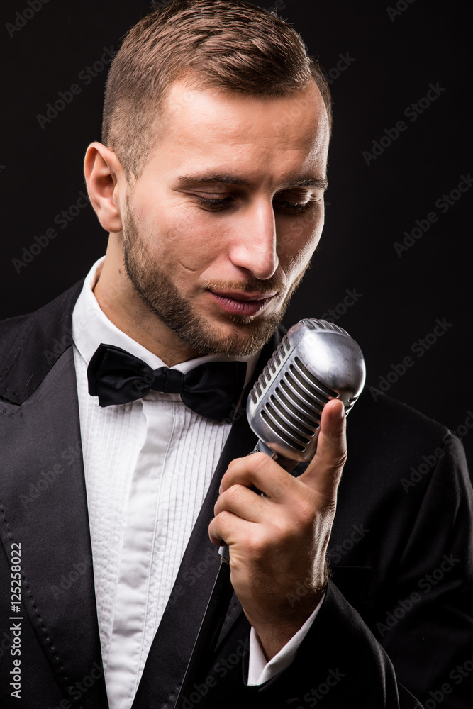 Naklejka premium Handsome Man in suit singing with the microphone and smile. Isolated on black background. Showman concept.