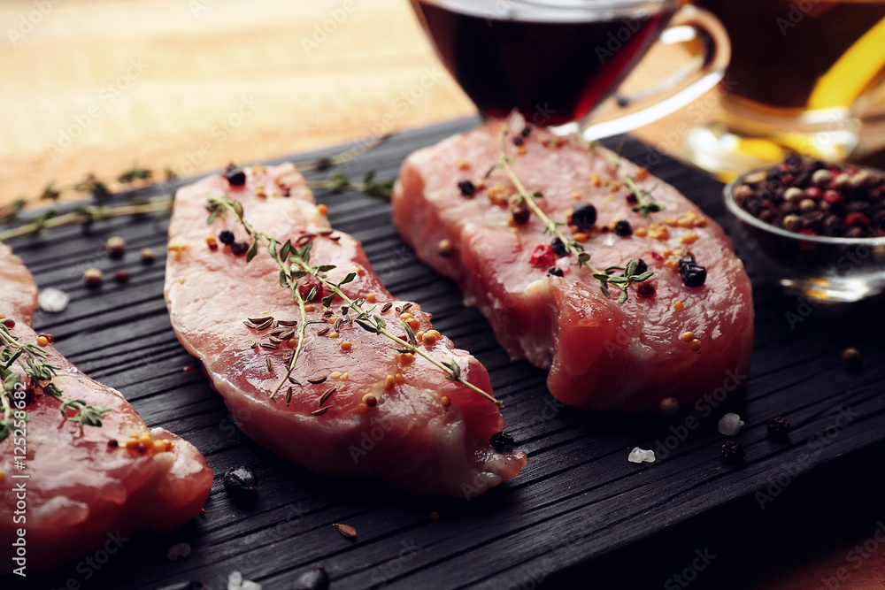 Raw steaks with herb and spices on wooden cutting board