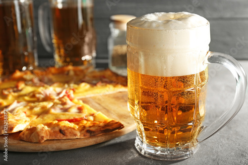 Glass of fresh beer and tasty pizza on background