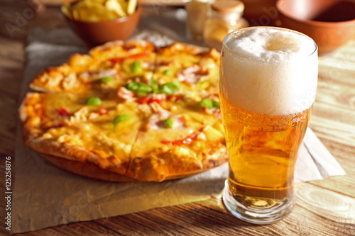 Glass of fresh beer and tasty pizza on background