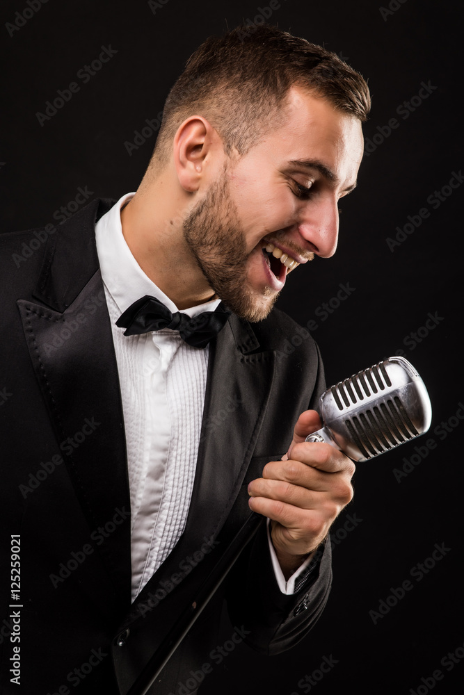 Naklejka premium Portrait of handsome man sing on microphone on black background. Singer concept.