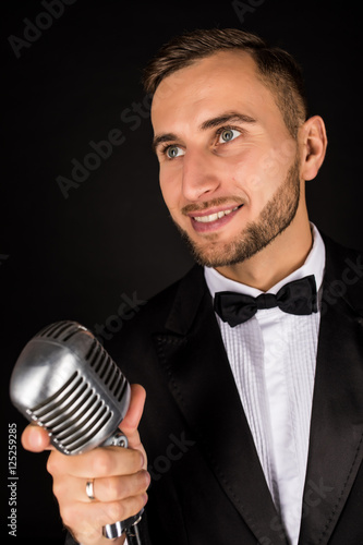 Portrait of handsome man sing on microphone on black background. Singer concept.