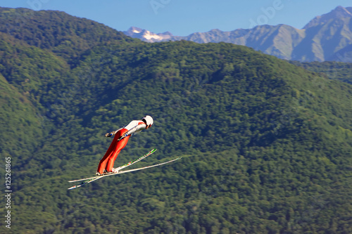 Professional skier flying from a ski jump on green mountains background at summer
