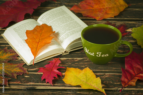 Autumn leaves, a book and a cup of hot tea on old boards