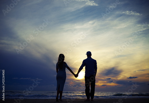Romantic couple holding hands while looking to the sunset