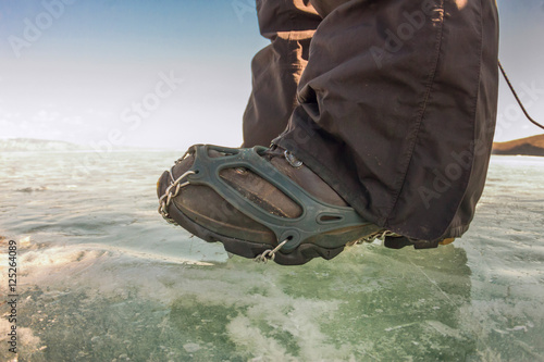Human legs in hiking boot in ice crampons on the texture Baikal