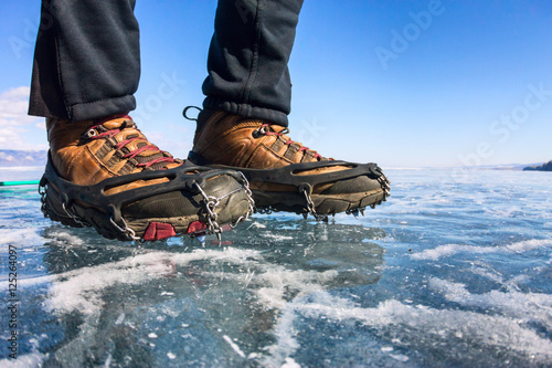 Human legs in hiking boot in ice crampons on the texture Baikal photo