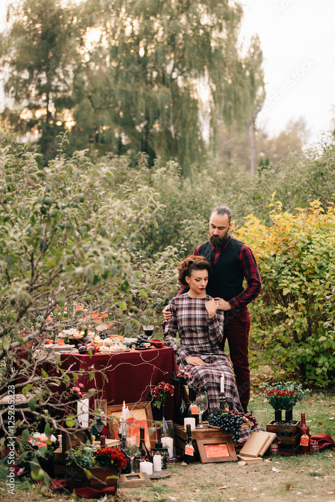 Beautiful bride is sitting at a decorated wedding table. Groom hugs bride. Beautiful bride is sitting at a decorated wedding table. Groom hugs bride.