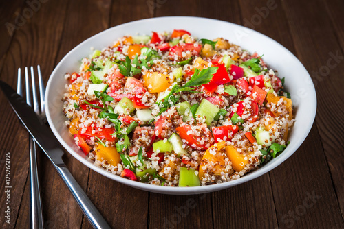 Fresh healthy salad with quinoa, colorful tomatoes, sweet pepper, cucumber and parsley on wooden background close up. Food and health. Superfood meal.