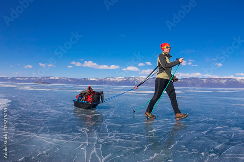 Girl with a sledge and trekking pole is on the ice of Lake Baika photo