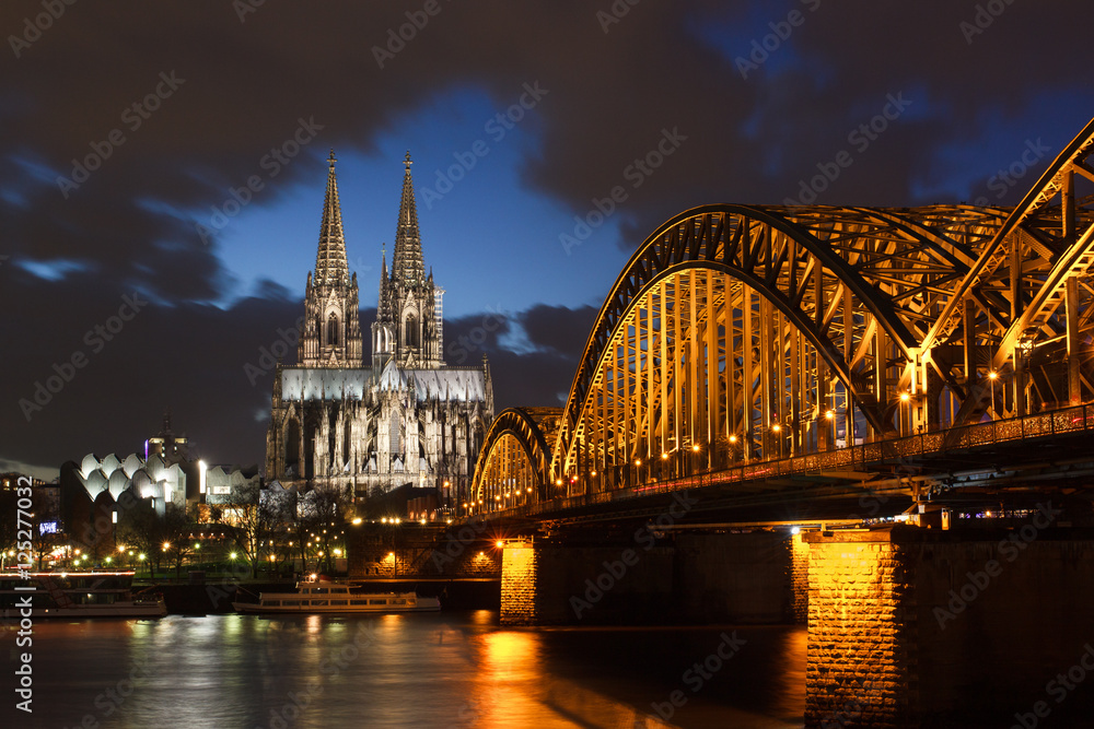 Illuminated cologne cathedral and bridge after sunset with blue sky and dark clouds