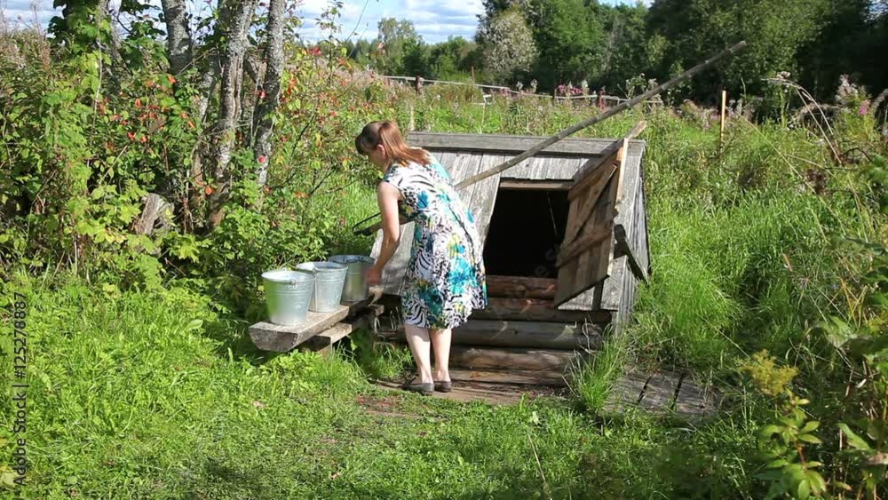 Young woman fills a bucket with water from the village water well Young woman fills a bucket with water from the village water well
