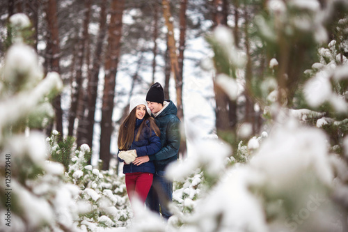 Winter love. Young couple in warm stylish clothing hugging in snowy winter forest