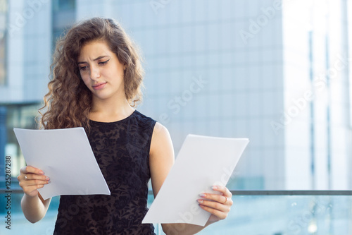 Curly girl holding a paper in his hand on the background of the business center, disappointment photo