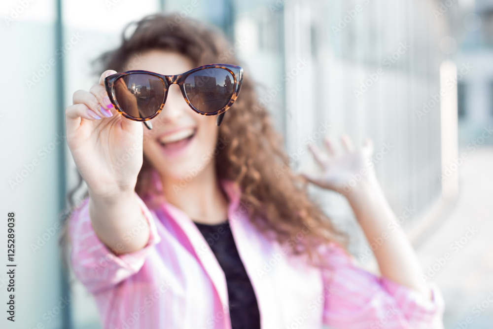 Curly girl smiling and holding a sunglasses. Focus on sunglasses. Curly girl smiling and holding a sunglasses. Focus on sunglasses.