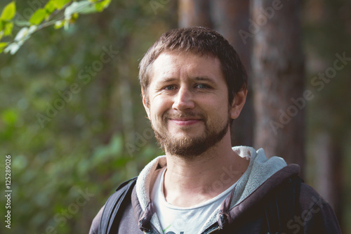 Adult strong man with beard smiling in forest