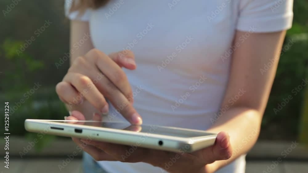 Young caucasian woman using digital pc tablet, touching and scrolling, outdoors in the garden, in nature. Sunset light, golden hour. Close-up shot Young caucasian woman using digital pc tablet, touching and scrolling, outdoors in the garden, in nature. Sunset light, golden hour. Close-up shot