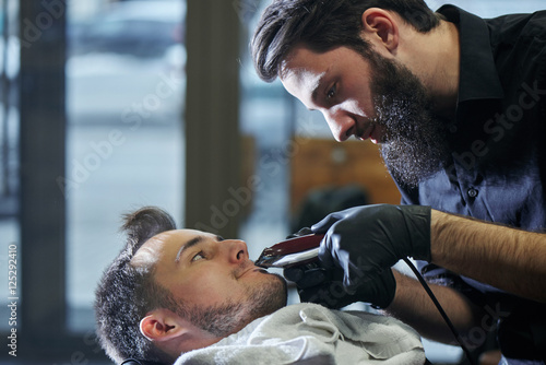 The Barber man in the process of cutting a mustache client electric clippers in the barbershop