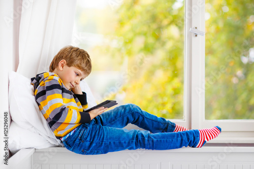  little school boy reading book or ebook by window