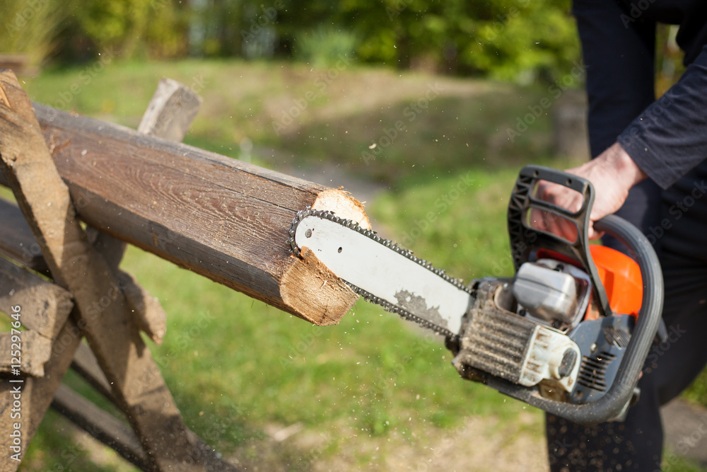 Man cutting some piece of wood by chainsaw on his huge garden du Man cutting some piece of wood by chainsaw on his huge garden du