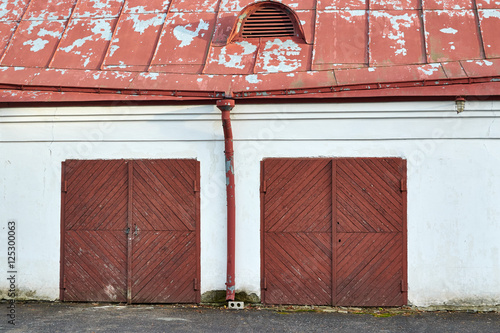 старое здание белого цвета с облезшей крышей и красными деревянными воротами