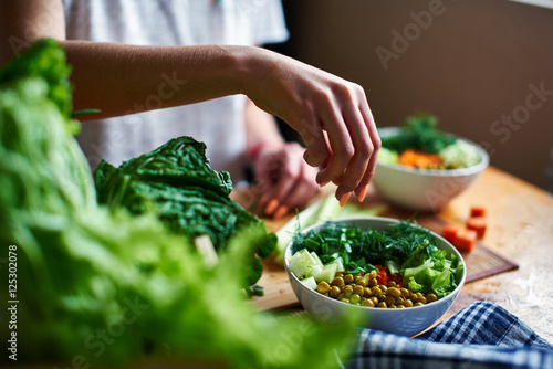 Photo Female hand pours green onions in a bowl with green peas, cucumbers, carrots, le