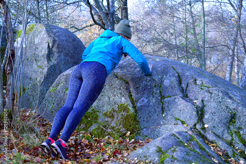 Woman working out in forest. Make push ups against big rock.